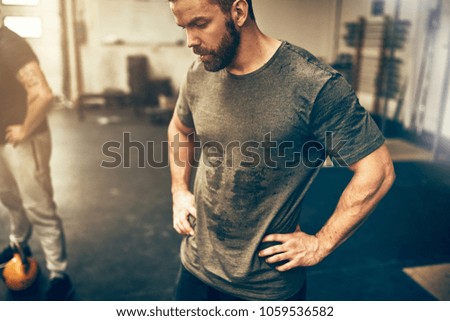 Fit young man in sportswear standing with his hands on his hips in a gym sweating after a workout session