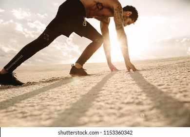 Fit Young Man In Starting Position Ready For Running. Athlete Ready To Start A Race Over Desert Sand With Sun Shining In Background.