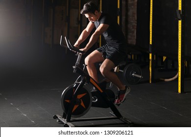 Fit Young Man Using Exercise Bike At The Gym. 