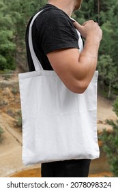 Fit Young Man Using White Blank Tote Bag Posing In Forest. Outdoor Minimal Clothing Product Apparel Style Business. Photo Template For Mockup, Print Store, E-commerce Shop, Branding Design Project.