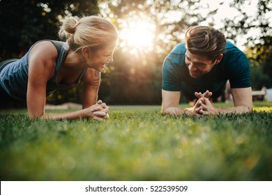 Fit young man and woman exercising in park. Smiling caucasian couple doing core workout on grass. - Shutterstock ID 522539509