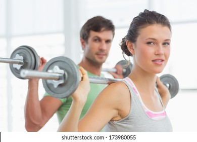 Fit Young Man And Woman Lifting Barbells In The Gym