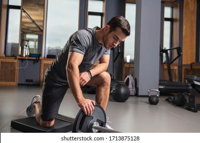 Fit young man working out with heavy weights standing on one knee pulling the barbell up - Powered by Shutterstock