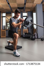 Fit young man working out with heavy weights standing on one knee pulling the barbell up
