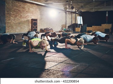 Fit young people doing pushups in a gym looking focused