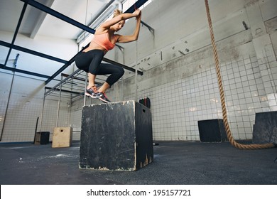 Fit young woman box jumping at a crossfit style gym. Female athlete is performing box jumps at gym.
