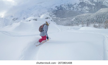 Fit young woman carves fresh powder snow while snowboarding off piste in Slovenia. Unrecognizable female tourist on winter vacation in the Julian Alps snowboards in the idyllic white backcountry.