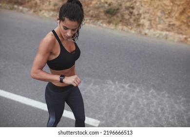 Fit Young Woman Checking Her Training Progress On A Smartwatch. Female Runner Having A Workout Session Along A Country Road In The Morning.