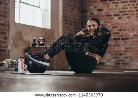 Fit young woman doing crunch workout to improve her abs. Smiling female in the gym doing sit-up exercise at gym.