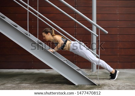 Fit young woman doing incline push ups exercise using urban stairs. City outdoor fitness workout.