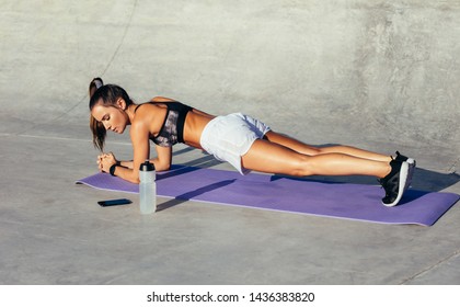 Fit young woman doing planks exercising outdoors in morning. Woman in sportswear working out on fitness mat.