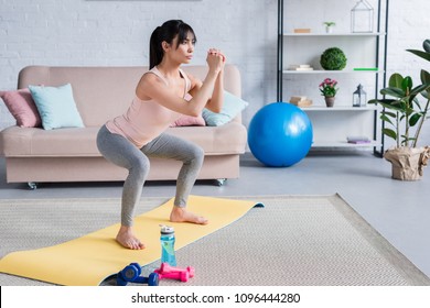 Fit Young Woman Doing Squats On Yoga Mat At Home