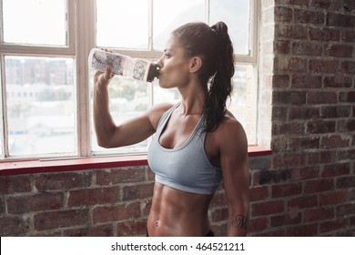 Fit young woman drinking water in the gym. Muscular woman taking break after exercise. - Powered by Shutterstock