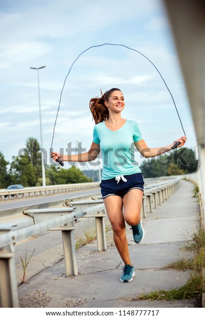 Fit young woman\
exercising with jump rope on a bridge. Active sport lifestyle in\
urban environment.