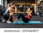 Fit young woman exercising with male personal trainer in gym on mat, doing abs workout in fitness gym, side view