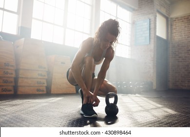 Fit young woman at gym tying her shoelace. Muscular female model getting ready for kettle bell workout. - Powered by Shutterstock