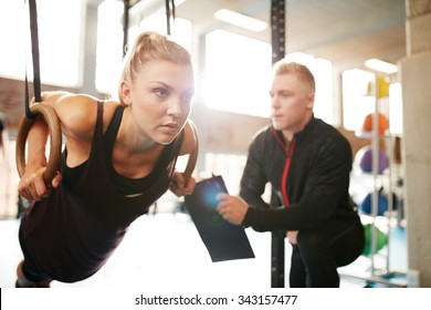 Fit young woman with her personal fitness trainer in the gym exercising with gymnastic rings - Powered by Shutterstock