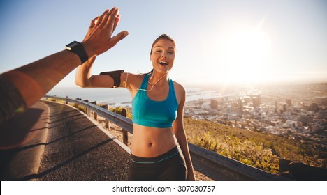 Fit young woman high fiving her boyfriend after a run. POV shot of runners on country road looking happy outdoors with bright sunlight.