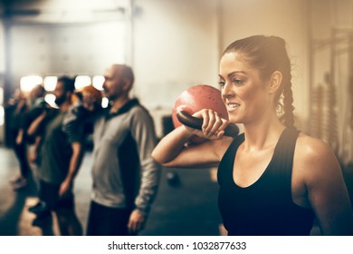 Fit young woman holding a dumbell while working out with other people during an exercise class at a gym