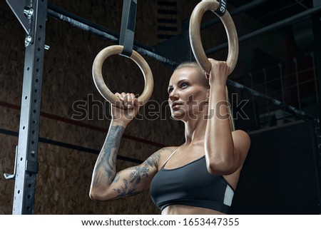 Fit young woman holding gymnastic rings at the gym and look confident. Fitness young woman looks inspired before starting workout.