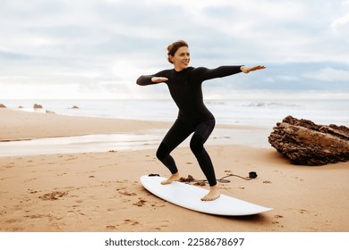 Fit young woman instructor demonstrating how to stand up on surfboard, preparing and practicing on surfboard on beach by seaside, free space - Powered by Shutterstock