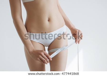 fit young woman measuring her waistline, grey blurred background with a space for your text.