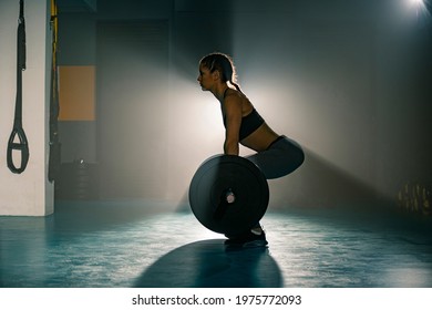 A fit young woman photographed from aside, doing a deadlift exercise in the gym.