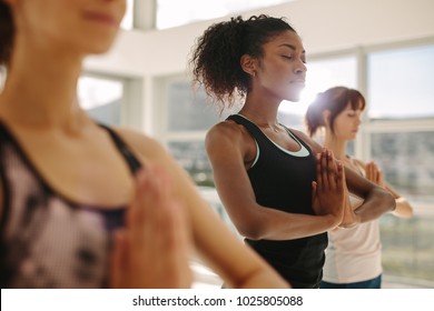 Fit young woman practice yoga with friends. Fitness female doing yoga meditation indoors in gym class.