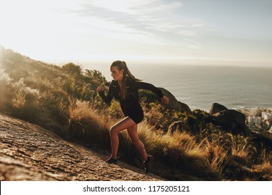 Fit Young Woman Running Up A Rocky Mountain Trail. Woman Trail Runner Training For Uphill Run.