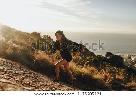 Fit young woman running up a rocky mountain trail. Woman trail runner training for uphill run.
