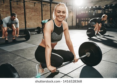 Fit Young Woman In Sportswear Smiling While Preparing For A Weight Lifting Class With Others At The Gym