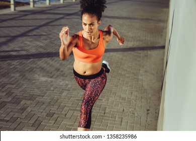 Fit young woman sprinting on the pavement. Female in sportswear running fast at the promenade.