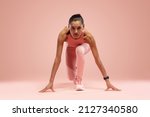 Fit young woman standing in start position over pink background. Sportswoman about to start a run.