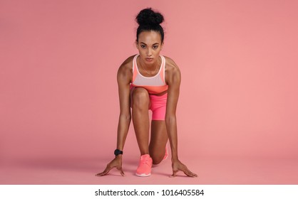 Fit Young Woman Standing In Start Position Over Pink Background. Sportswoman About To Start A Run.