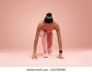 Fit Young Woman Standing In Start Position Over Pink Background. Sportswoman About To Start A Run.