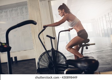 Fit young woman using exercise bike at the gym. Fitness female using air bike for cardio workout at crossfit gym. - Powered by Shutterstock