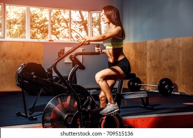 Fit young woman using exercise bike at the gym. Fitness female using air bike for cardio workout at crossfit gym. - Powered by Shutterstock