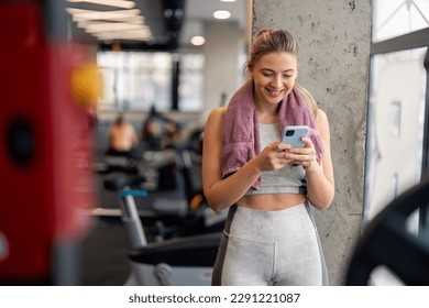 Fit young woman using mobile phone in gym to watch virtual workout tutorial video to improve her fitness workout exercise  Motivated sportswoman watching online fitness tutorial smartphone in gym 