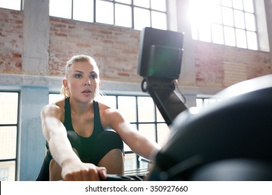 Fit Young Woman Working Out On A Rowing Machine At The Gym. Caucasian Female Doing Cardio Exercise In Fitness Club.