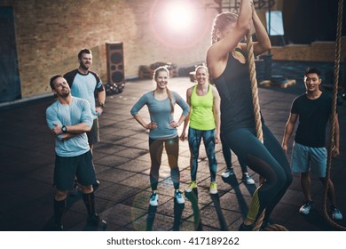 Fit young women climbing a rope in a gym with people on the floor watching - Powered by Shutterstock