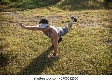 A Fit And Youthful Asian Man Performs Bird Dogs On The Grass Of An Open Field. Lower Back And Ab Workout.