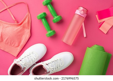 Fitness accessories concept. Top view photo of pink sports bra green dumbbells white sneakers exercise mat bottle and resistance bands on isolated pink background