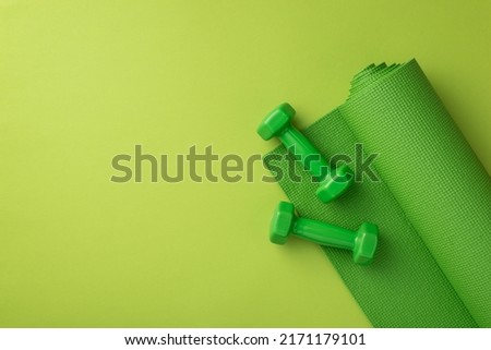 Fitness accessories concept. Top view photo of green sports mat and dumbbells on isolated green background with copyspace