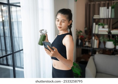 Fitness asian woman using smart phone and drinking organic green smoothie fruit detox for diet after workout exercise
training healthy lifestyle. - Powered by Shutterstock