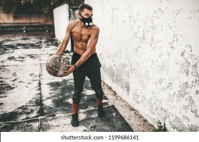 Fitness Athlete Male Doing Exercises With Medicine Ball In Mask On Concrete Background Outdoor With Copy Space For Your Advertising. Caucasian Shirtless Sportsman Doing Workout 