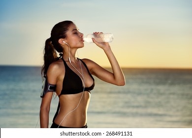 Fitness beautiful woman drinking water and sweating after exercising on summer hot day in beach. Female athlete after workout - Powered by Shutterstock