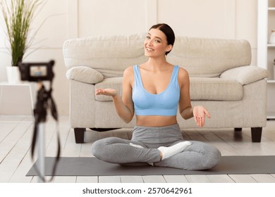 Fitness Blogging. Cheerful Blogger Girl Making Video For Online Yoga Course Sitting On Mat At Home. Selective Focus
