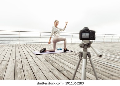 Fitness blogging. Young healthy sport woman records yoga workout on camera with tripod showing how to perform asana poses on the beach. Vlogging - Powered by Shutterstock