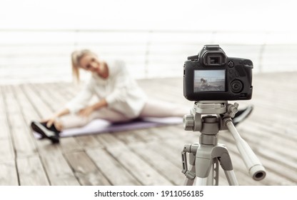 Fitness blogging. Young healthy sports woman recording workout on camera with tripod and showing how to do exercise on the beach. Vlogging - Powered by Shutterstock