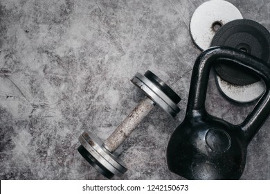 Fitness Or Bodybuilding Concept Background. Old Iron Dumbbells And Kettlebell On Grey, Conrete Floor In The Gym.  Top View. Healthz Lifestyle.